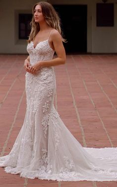 a woman in a white wedding dress standing on a brick floor with her arms crossed