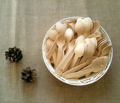 wooden spoons and pine cones in a white bowl on a beige tablecloth next to an evergreen cone