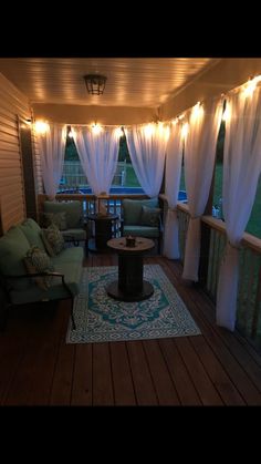 an outdoor living room with white curtains and lights on the ceiling, couches and coffee table