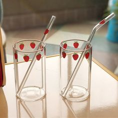 two glass cups with strawberries on them sitting on a table next to each other