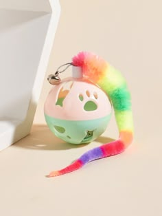 a small toy with a rainbow tail on it's head next to a white wall