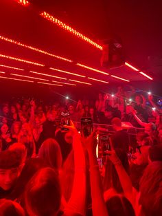 a large group of people in a room with red lights and one person holding up a cell phone