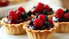 small tarts with berries and blueberries are on a white platter, ready to be eaten