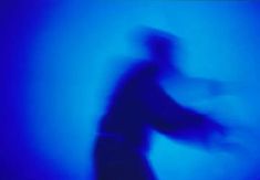 a blurry image of a man holding a skateboard in the dark blue light