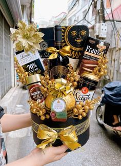 a person is holding a wine and chocolates gift basket in the middle of an alleyway