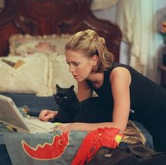 a woman laying on her bed using a laptop computer with a black cat sitting next to her