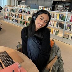 a woman sitting at a table with a laptop in front of her and bookshelves behind her