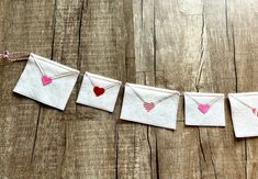 some small envelopes are hanging from a string on a wooden surface, with hearts painted on them