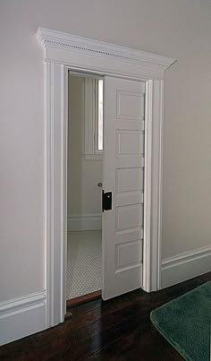 an empty living room with white walls and wood flooring, looking into the hallway