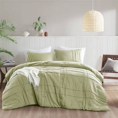 a bed with green comforter and pillows in a room next to a plant on the wall