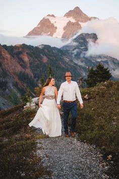 a bride and groom walking down a path in the mountains at their wedding day with snow capped peaks behind them