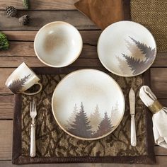 a place setting with pine trees painted on the plates and silverware, napkins and forks