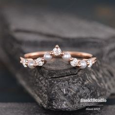 a rose gold ring with white pearls and diamonds on top of a black stone rock