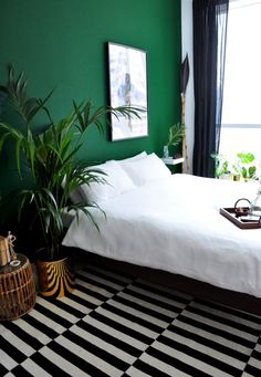 a bedroom with green walls and black and white checkered flooring, potted plants in front of the bed