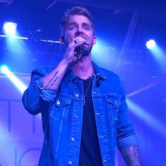 a man with tattoos on his arm singing into a microphone in front of blue lights