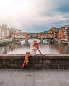 a woman sitting on the edge of a wall next to a river