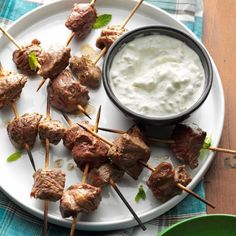 skewered meat and dip on a plate next to a bowl of yogurt