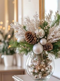 a vase filled with christmas decorations and pine cones on top of a table next to a mirror