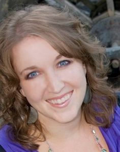 a smiling woman with blue eyes and brown hair is posing for a photo in front of some rocks