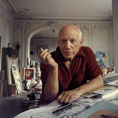 an older man sitting at a table with papers and pens in his hand, looking off into the distance