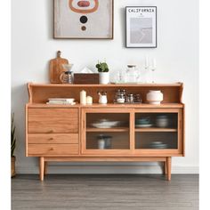 a wooden sideboard with glass doors and plates on it in front of a white wall