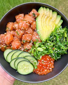 a person holding a black bowl filled with different types of food and veggies