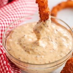 a fried onion ring dipping sauce in a small glass bowl on a red and white checkered napkin