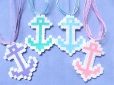 four different colored cross and anchor ornaments on a blue background with pink, purple, and white ribbons