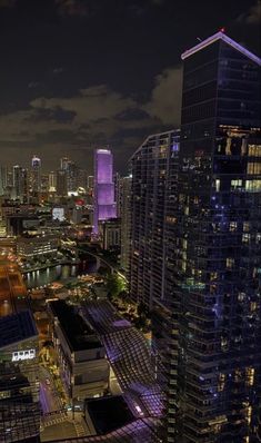 the city skyline is lit up at night with skyscrapers in the foreground and other high rise buildings