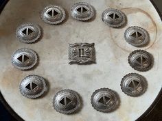 a bunch of silver buttons sitting on top of a white plate with an emblem in the middle