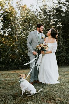 a bride and groom standing in the grass with their dog