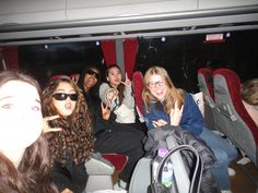 group of young women sitting in seats on bus with one pointing at camera and the other holding up peace signs