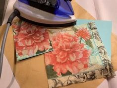 an iron on top of some fabric and paper with pink flowers printed on the side