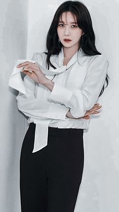 a woman in white shirt and black pants leaning against wall with her hands on her hips