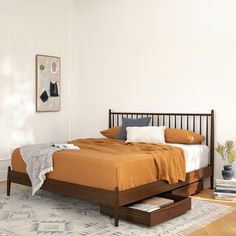 a bed with an orange blanket on top of it next to a white wall and wooden floor