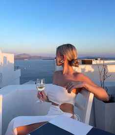 a woman sitting at a table with a glass of wine in her hand and looking out over the water