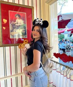 a woman holding a donut in her right hand and mickey mouse ears on her head