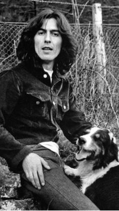 an old black and white photo of a man sitting with his dog in front of a fence