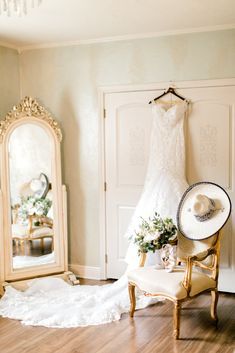 a wedding dress hanging on the wall next to a mirror and chair in a room