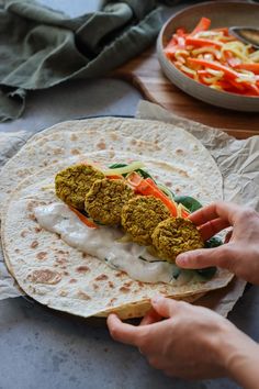 a person is holding a burrito with meat and vegetables in the background on a table