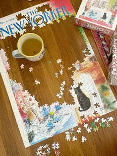 a cup of tea sits on the floor next to puzzles and books that have been put together