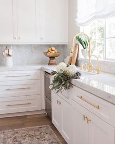 a white kitchen with marble counter tops and gold hardware on the cabinetry, along with an area rug