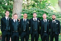 a group of men standing next to each other in front of a lush green forest