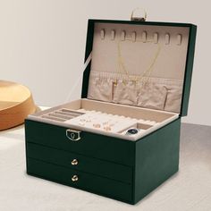 an open green box with jewelry inside on a white table next to a wooden bowl