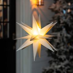 an origami star hanging from the ceiling next to a christmas tree with lights on it