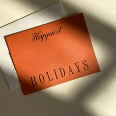 an orange card with the words happfest holidays written on it sitting next to a white envelope