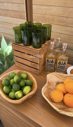 limes and oranges in wooden bowls next to bottles of alcohol on a table