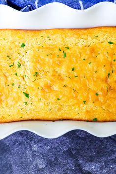 a rectangular casserole dish with cheese and parsley on top, next to a blue towel