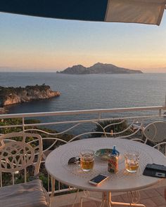 an outdoor table with drinks on it overlooking the ocean