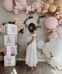 a pregnant woman standing in front of balloons and garlands with her hands on her stomach